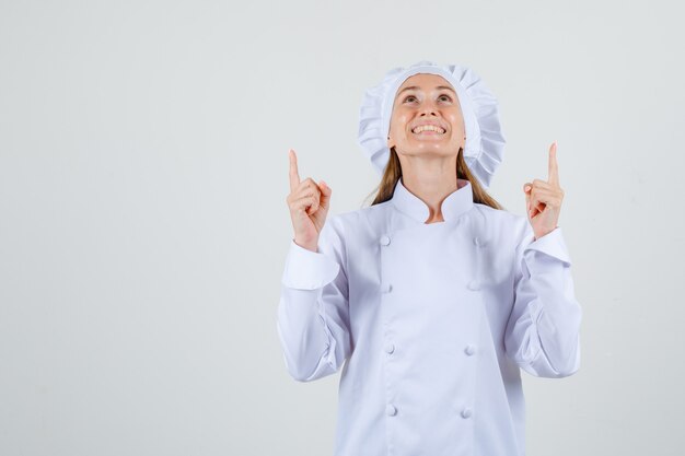 Female chef pointing up fingers in white uniform and looking happy. front view.