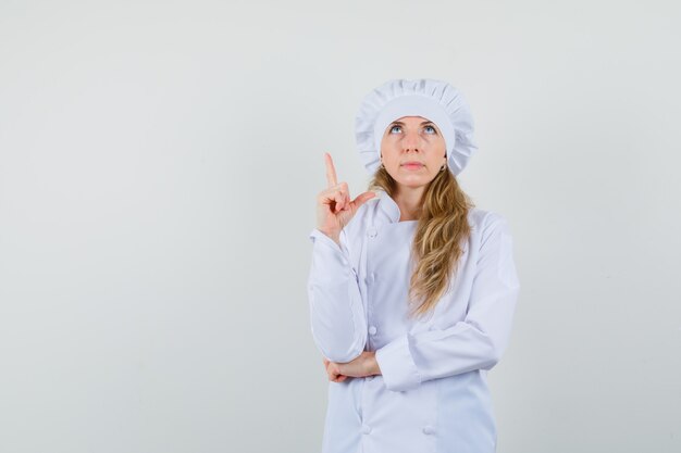 Female chef pointing up in white uniform and looking focused. 