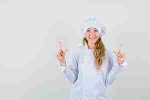 Foto gratuita cuoco unico femminile che indica in su in uniforme bianca e che sembra felice