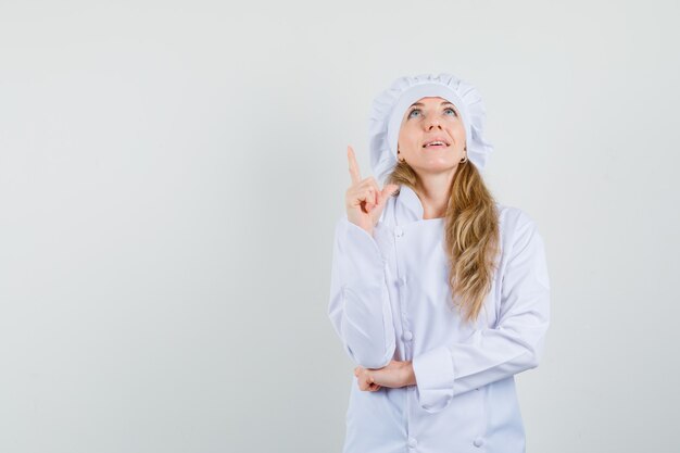 Female chef pointing up in white uniform and looking hopeful 