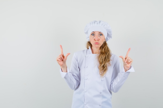 Female chef pointing up in white uniform and looking scared 