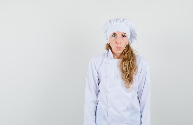 Female chef pouting lips, looking at camera with squint eyes in white uniform and looking funny. 