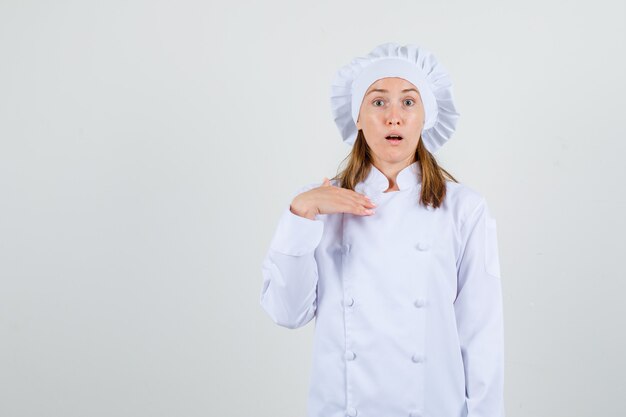 Female chef showing 'me?' gesture in white uniform and looking confused
