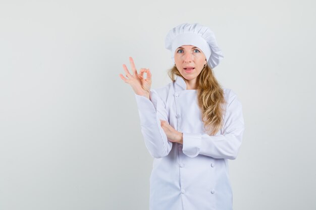 Female chef showing ok gesture in white uniform and looking pleased 