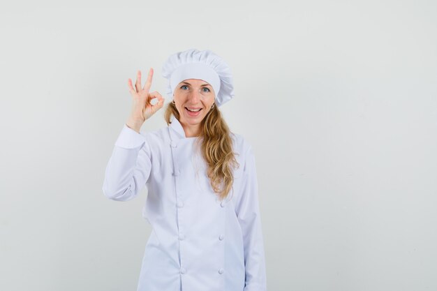 Female chef showing ok gesture in white uniform and looking satisfied. 