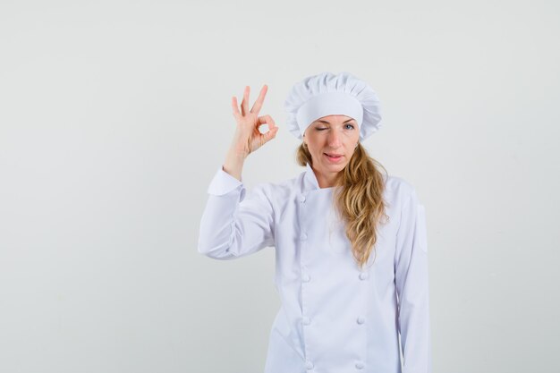 Female chef showing ok sign and winking eye in white uniform 