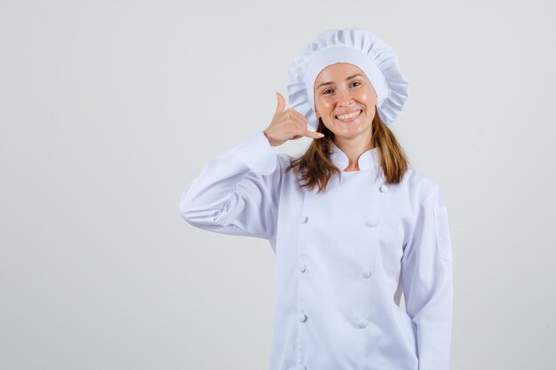 Female chef showing phone gesture in white uniform and looking glad. front view.