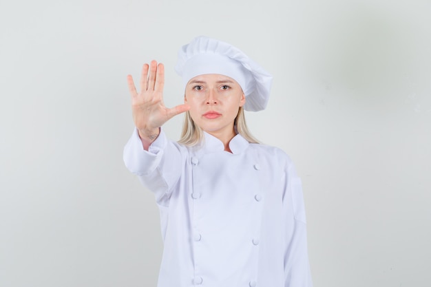 Female chef showing stop gesture in white uniform and looking serious.