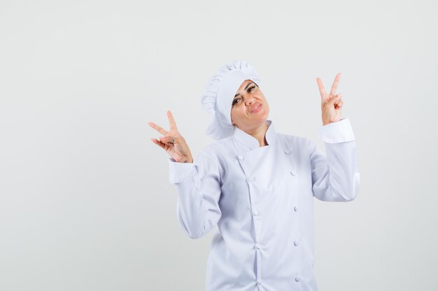 Female chef showing v-sign in white uniform and looking cheery. 