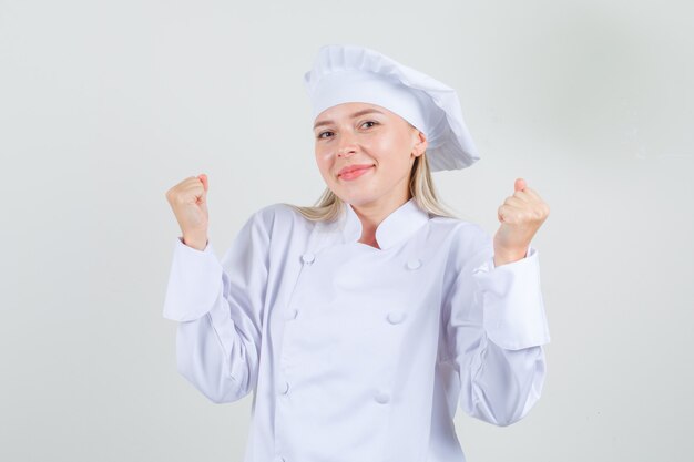 Female chef showing winner gesture and smiling in white uniform 