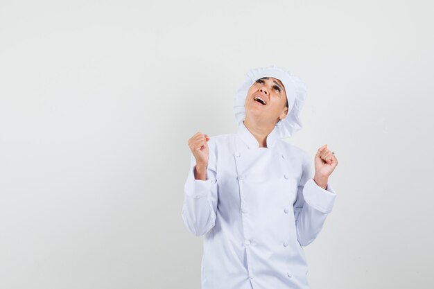 Female chef showing winner gesture while looking up in white uniform