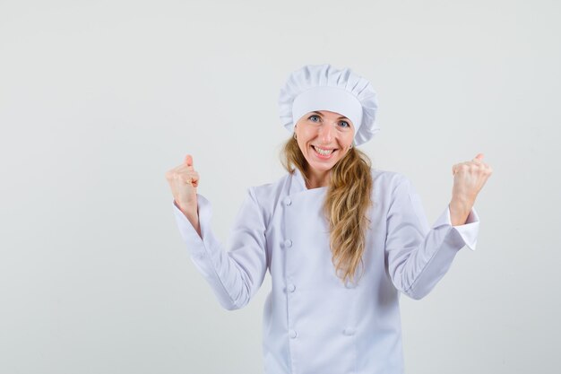 Женщина-шеф-повар показывает жест победителя в белой форме и выглядит счастливым