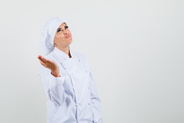 Женщина-шеф-повар в белой униформе разводит ладонь и смотрит с надеждой
