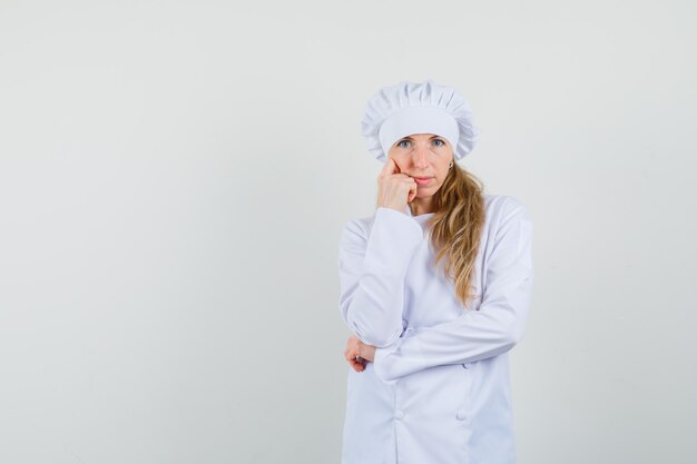 흰색 유니폼과 초점을 찾고 생각 포즈에 서있는 여성 요리사.
