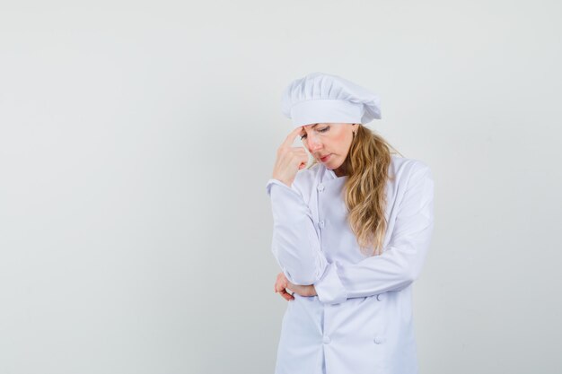 Female chef standing in thinking pose in white uniform and looking sad 