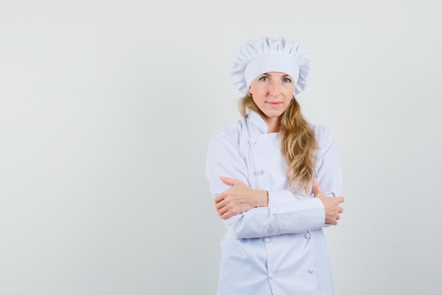 Female chef standing with crossed arms in white uniform and looking confident 