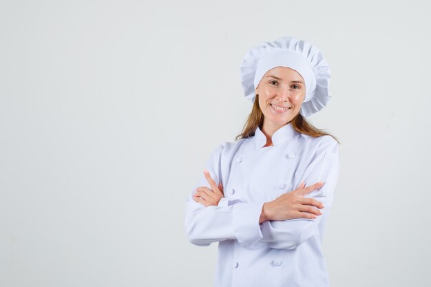 Female chef standing with crossed arms in white uniform and looking happy