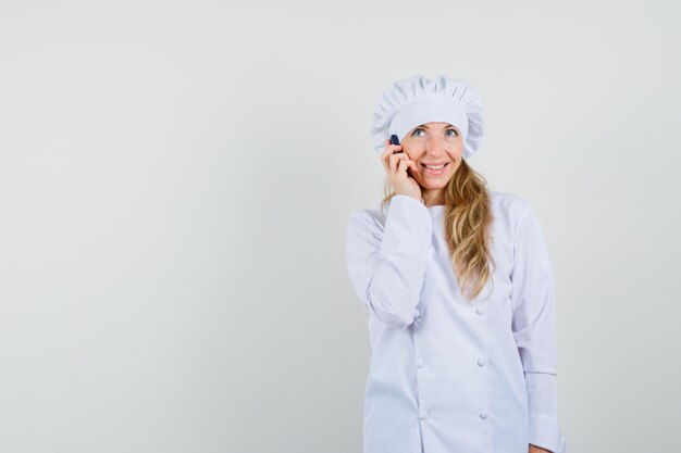 Женщина-шеф-повар разговаривает по мобильному телефону в белой форме и радуется