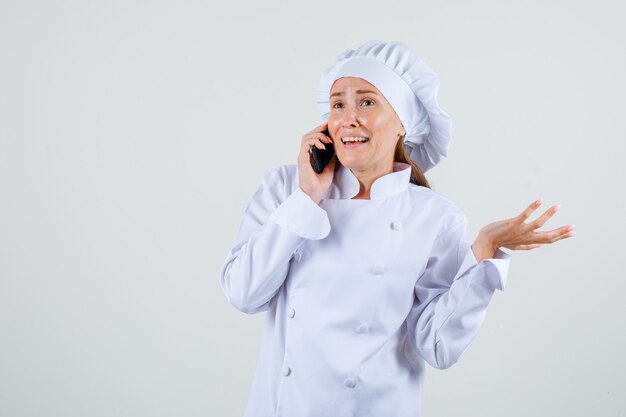 흰색 유니폼에 휴대 전화에 대 한 얘기 하 고 쾌활 한 찾고 여성 요리사. 전면보기.