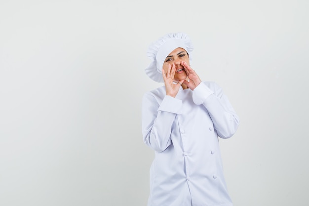 Female chef telling secret with hands near mouth in white uniform 