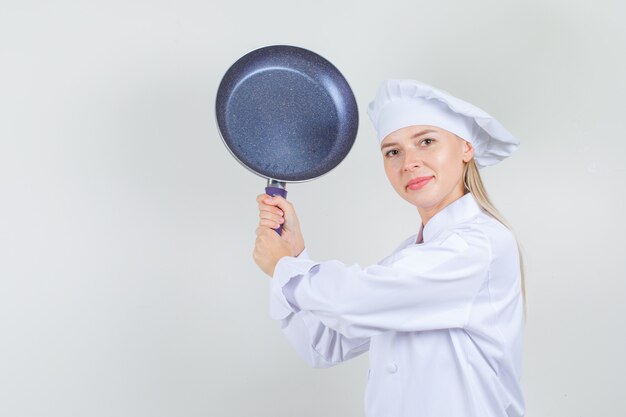 흰색 유니폼에 프라이팬으로 위협하고 재미 보는 여성 요리사