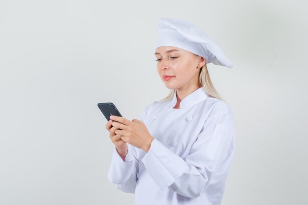 Female chef typing on smartphone and smiling in white uniform