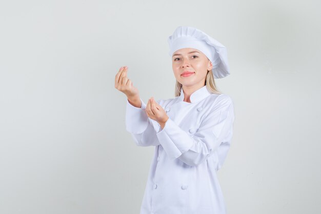 Female chef in white uniform doing money gesture and smiling 