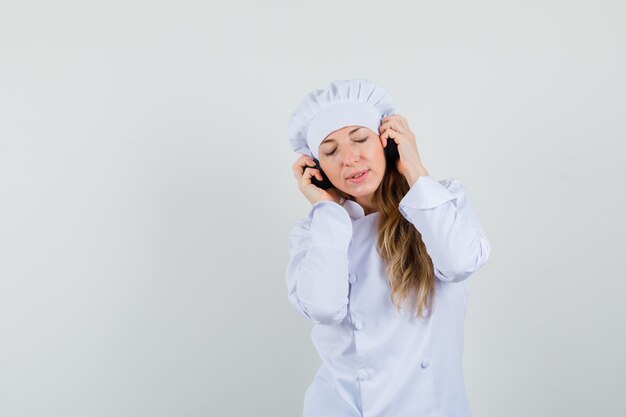 Female chef in white uniform enjoying music with headphones 