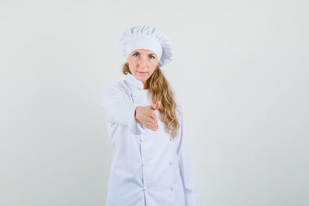 Женщина-шеф-повар в белой форме протягивает руку для рукопожатия и выглядит нежной