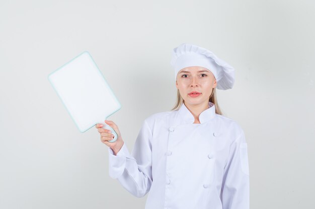 Женщина-шеф-повар в белой форме держит разделочную доску и улыбается