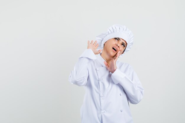 Female chef in white uniform holding hand near mouth and looking curious