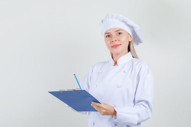 Female chef in white uniform holding pencil and clipboard and looking cheery 