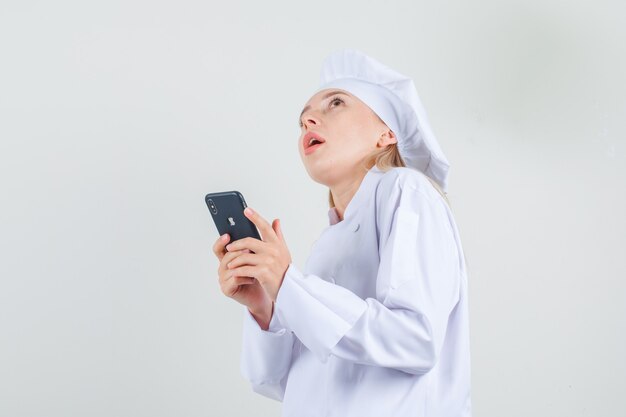 Female chef in white uniform holding smartphone and thinking .