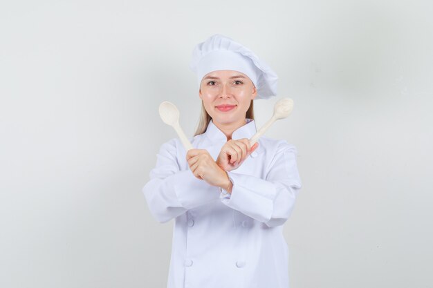 Female chef in white uniform holding wooden spoons and looking cheery 