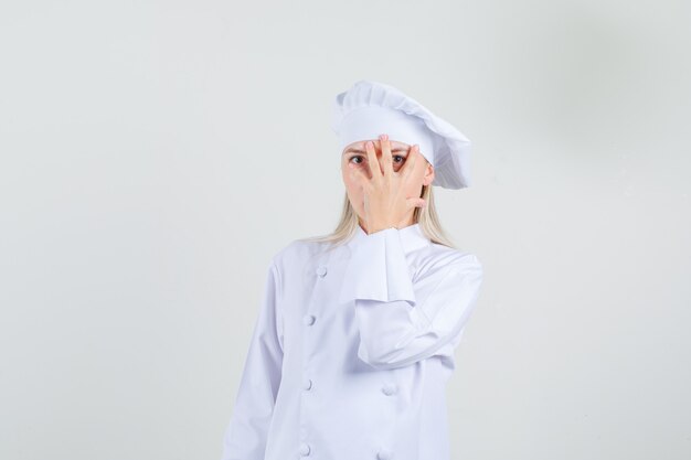 손가락을 통해보고 교활한 흰색 유니폼을 입은 여성 요리사