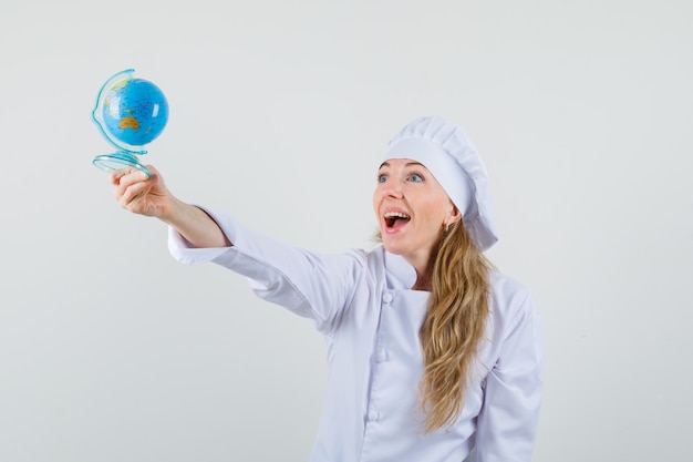 Free photo female chef in white uniform looking at world globe and looking happy