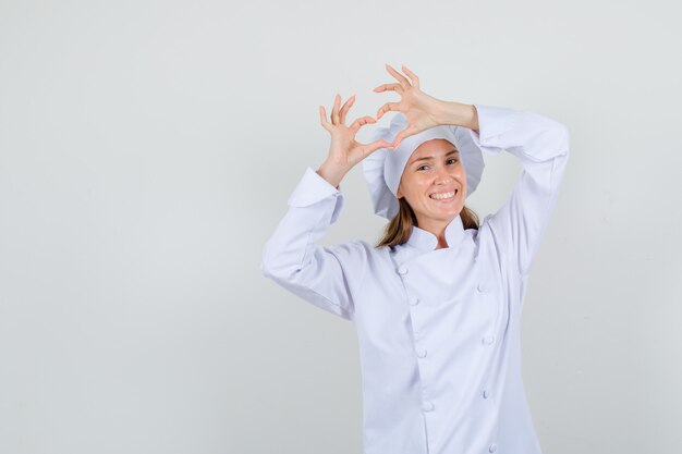 Female chef in white uniform making heart shape and looking happy