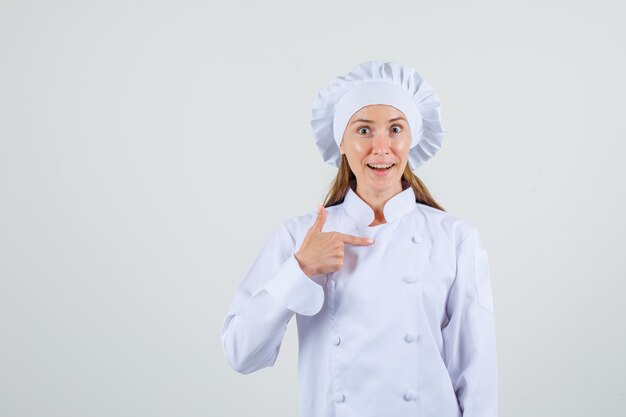 Female chef in white uniform pointing finger at herself and looking surprised