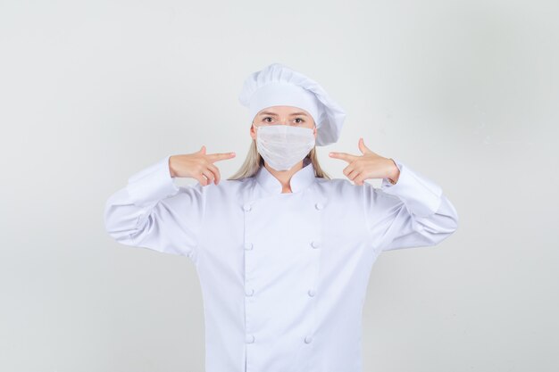 Female chef in white uniform pointing fingers at medical mask 