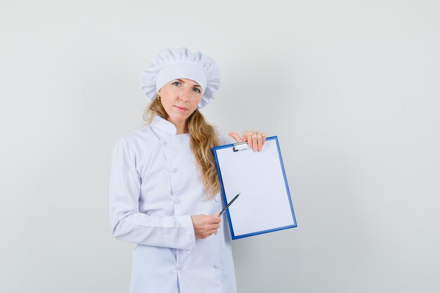 Female chef in white uniform pointing pen a clipboard and looking sensible 