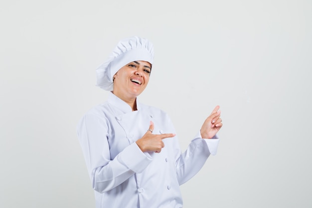 Female chef in white uniform pointing to the side and looking glad