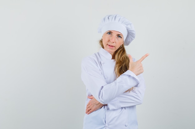 Женщина-шеф-повар в белой униформе указывает в сторону пальцем вверх и выглядит уверенно