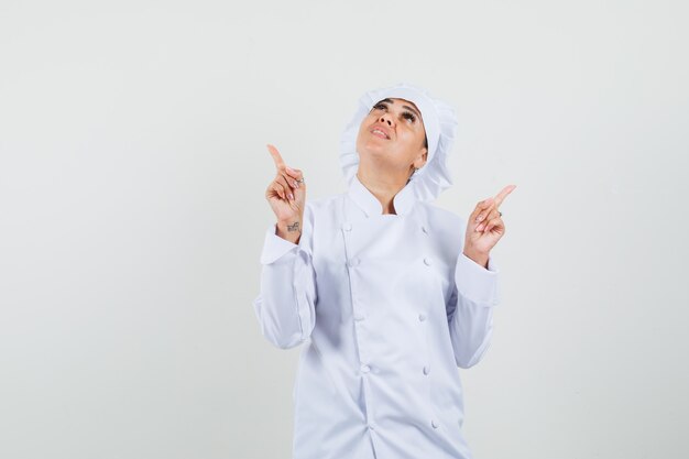 Женщина-шеф-повар в белой форме указывает вверх и смотрит сосредоточенно