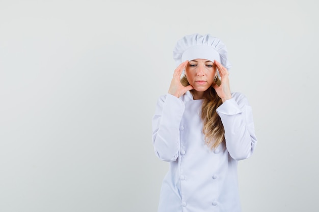 Foto gratuita cuoco unico femminile in uniforme bianca che sfrega le tempie e sente il mal di testa e sembra esausto