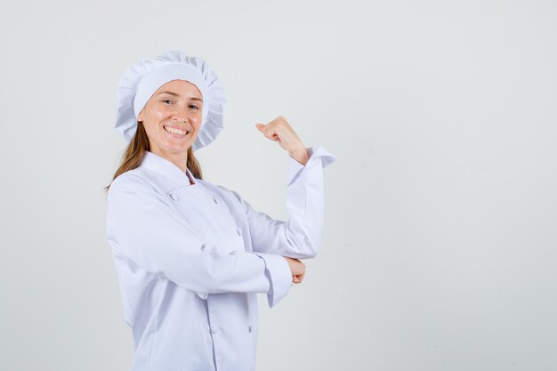 Female chef in white uniform showing arm with clenched fist and looking cheerful