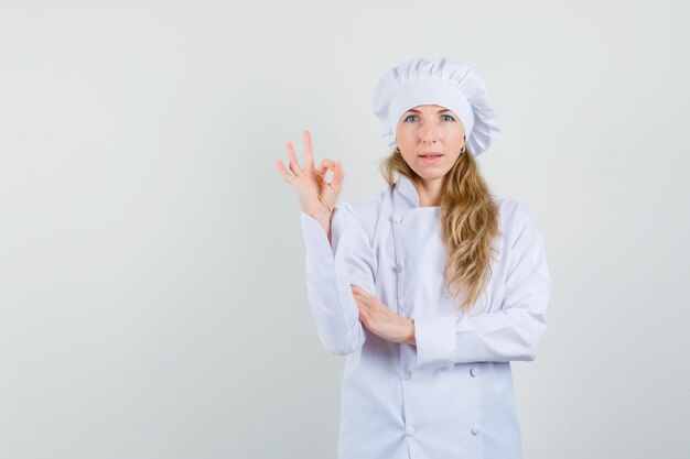 Женщина-шеф-повар в белой униформе показывает жест `` ОК '' и выглядит довольным