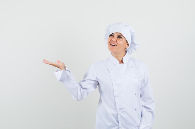 Female chef in white uniform spreading palm aside and looking hopeful