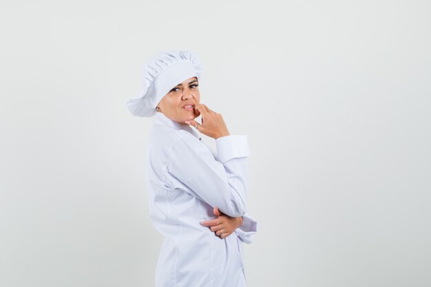 Female chef in white uniform standing in thinking pose and looking cheerful .