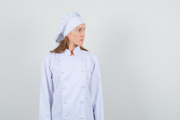 Женщина-шеф-повар в белой форме смотрит в сторону и выглядит серьезно