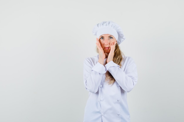 Female chef in white uniform touching her face skin and looking delicate 